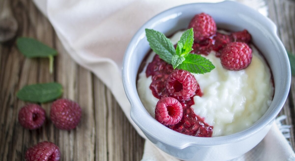 Milchreis mit Himbeeren / runde Schüssel / Tuch / Untergrund Holz / Nahaufnahme/ Draufsicht