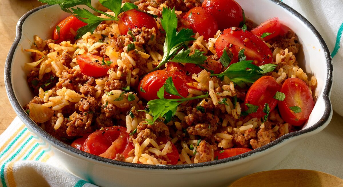 Weiße Schüssel gefüllt mit Reis, Hackfleisch und kleinen Tomaten. 