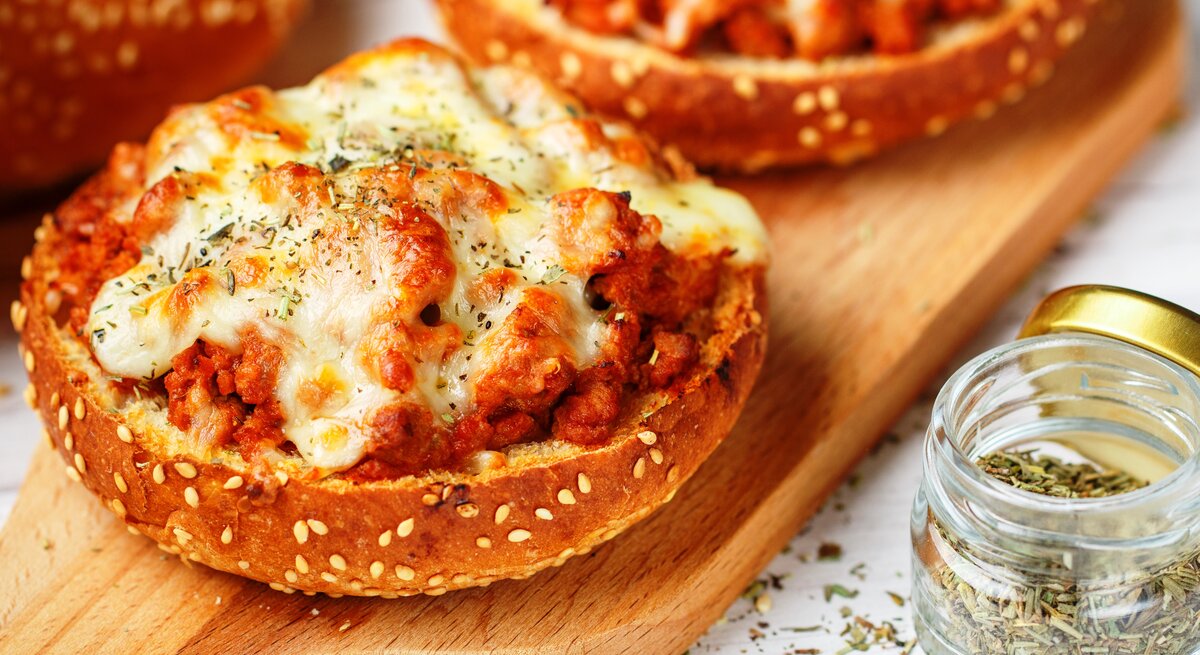 Pizzabrötchen mit Hackfleisch und Käse auf Holzbrett. 