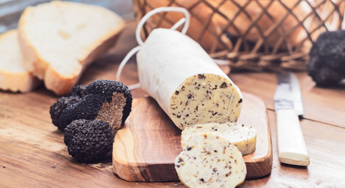 Angeschnittene Rolle Trüffelbutter arrangiert auf einem Holzbrett. 
