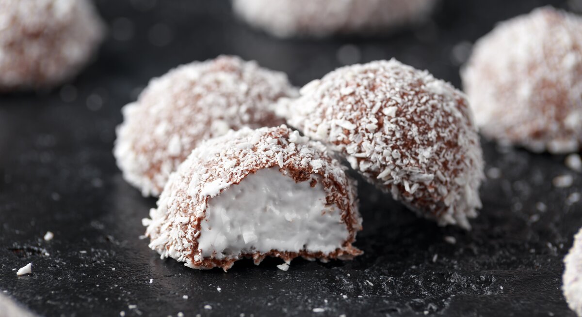 Schokoladenpralinen mit Kokosraspel bedeckt auf dunklem Untergrund.