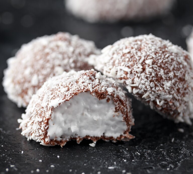 Schokoladenpralinen mit Kokosraspel bedeckt auf dunklem Untergrund. | © Getty Images/ DronG