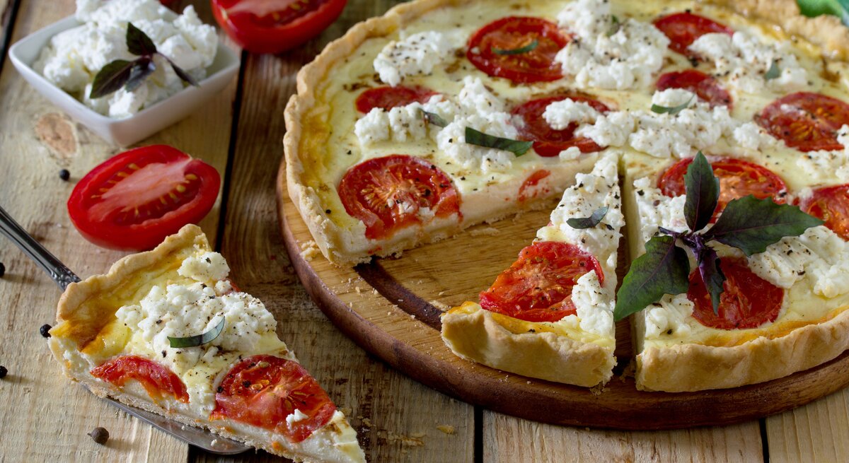 Tomaten-Ricotta-Quiche mit Kräutern auf hölzernem Untergrund. 