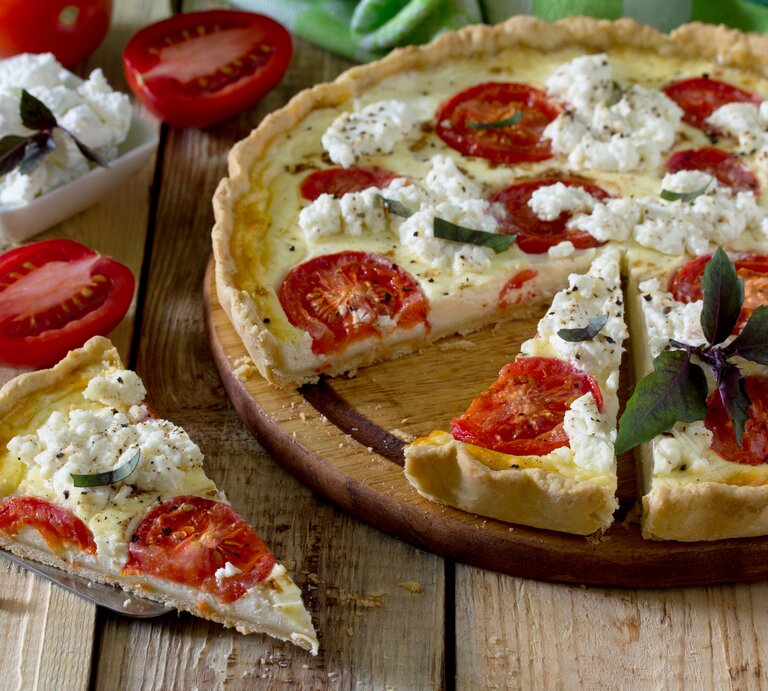 Tomaten-Ricotta-Quiche mit Kräutern auf hölzernem Untergrund.  | © GettyImages/elena_hramowa