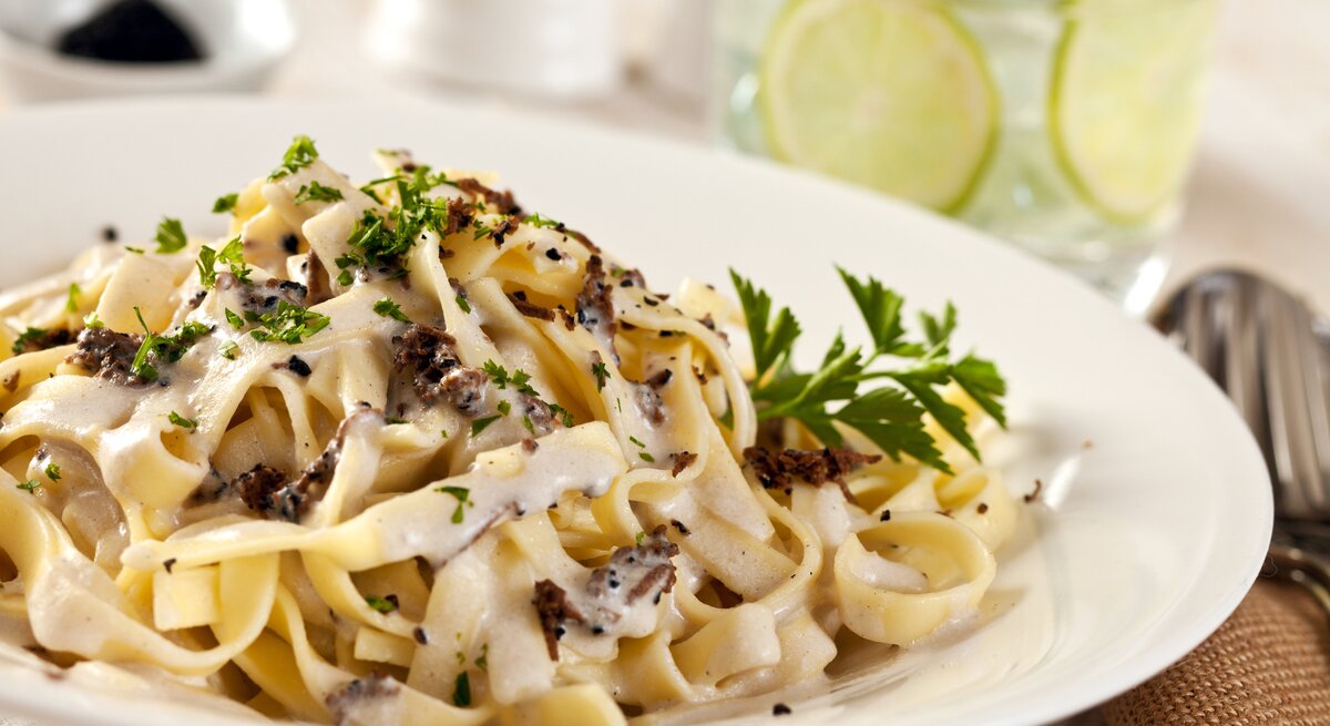 Ein weißer Teller, darauf Pasta mit Trüffeln, Parmesan und cremiger Soße. 