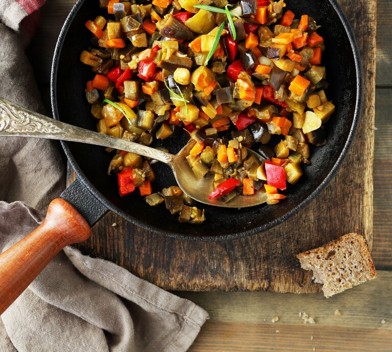 Eine schwarze Pfanne mit Holzgriff und dem Gericht auf einem rustikalen Holztisch. Alles direkt von oben fotografiert. | © iStock/Olha_Afanasieva