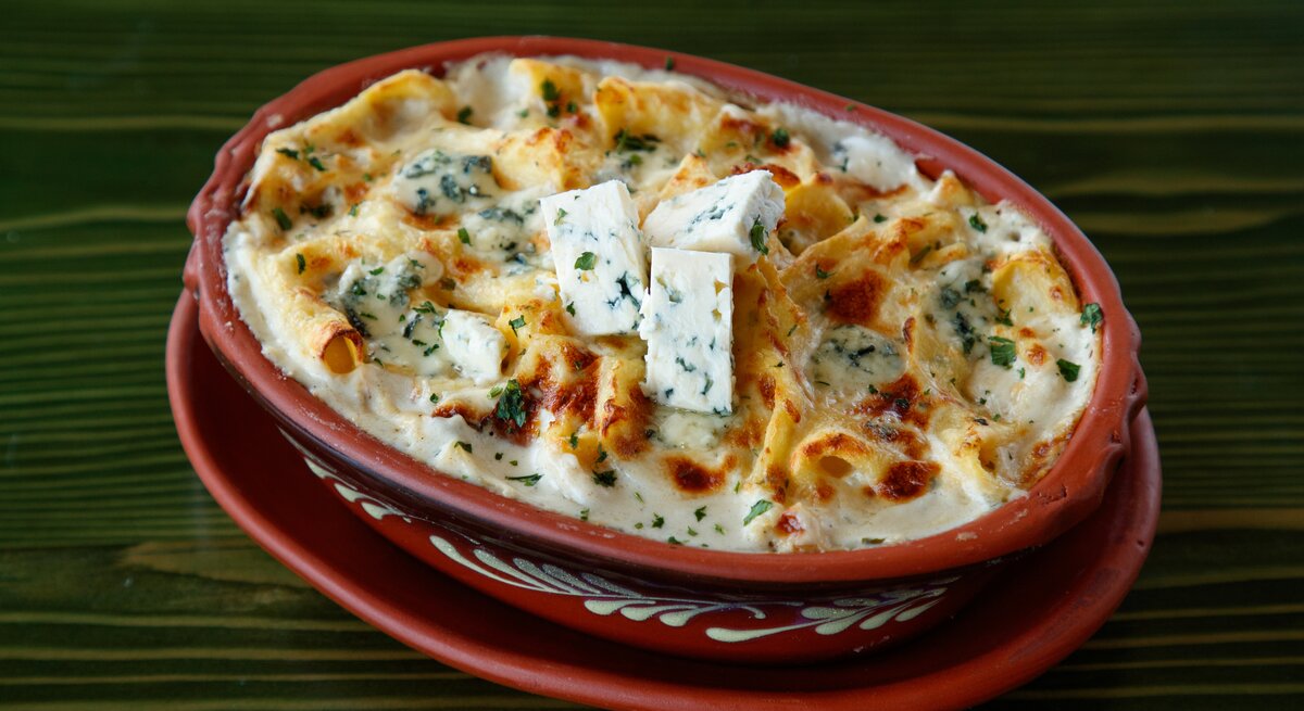 Gorgonzola-Nudelauflauf in Auflaufform auf grünem Untergrund.