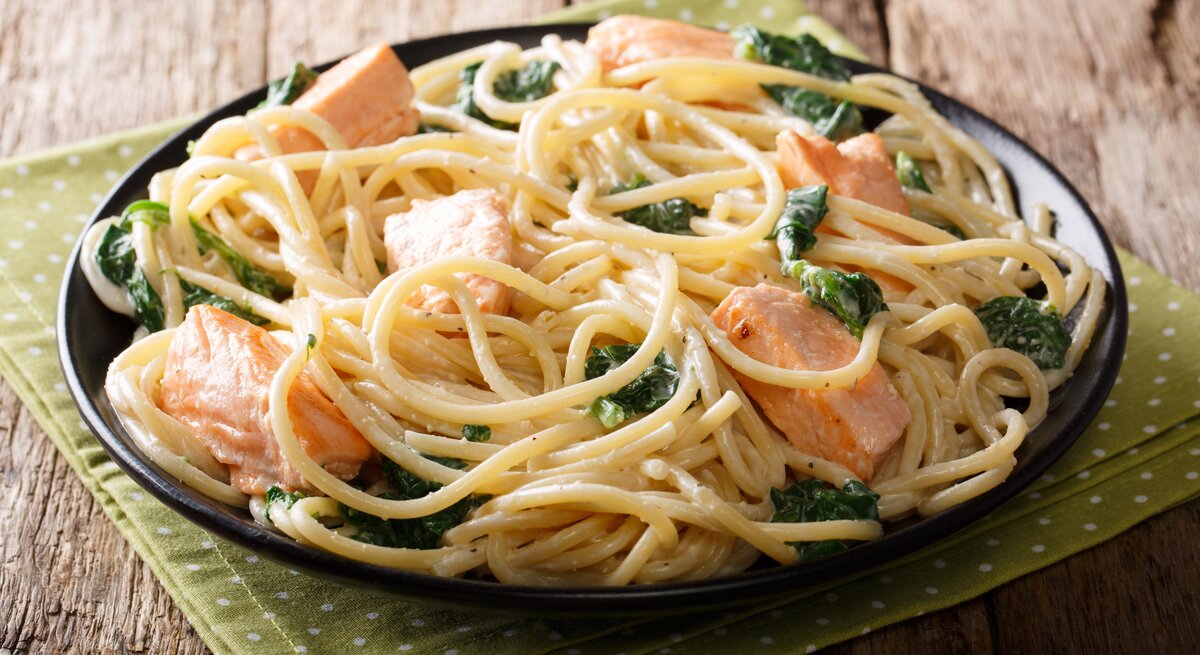 Seitliche Ansicht auf einen Teller mit Spaghetti mit Lachs in Spinat-Sahnesoße auf Holztisch.
