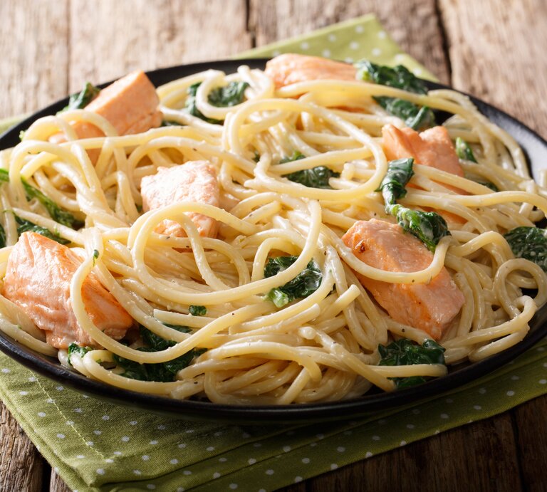 Seitliche Ansicht auf einen Teller mit Spaghetti mit Lachs in Spinat-Sahnesoße auf Holztisch. | © iStock/ALLEKO