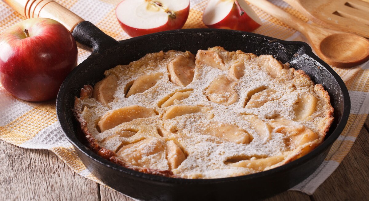 Apfelpfannkuchen in gusseiserner Pfanne auf gelb-weiß karriertem Tischtuch.