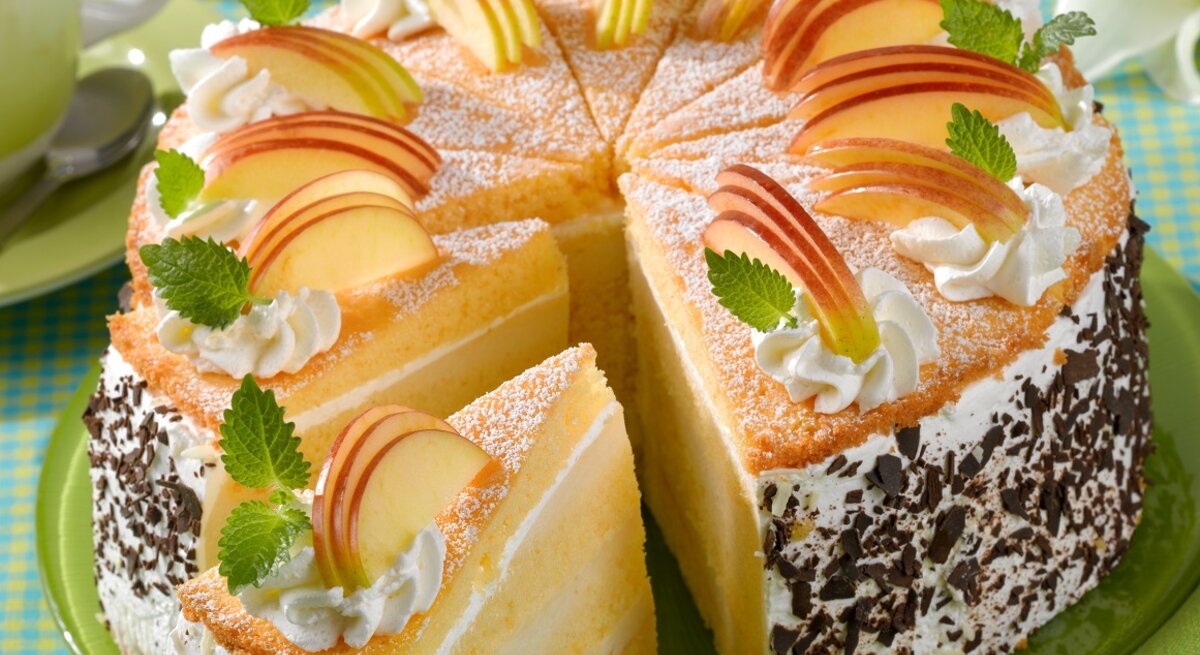 Die Apfelcreme-Schichttorte auf einem Tisch mit hellgrüner Tischdecke von schräg oben fotografiert.