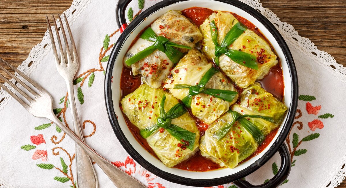 Frisch gemachte vegetarische Kohlrouladen in einem Topf / jede ist mit einem breitem band verschnürt / Untergrund besticktes Tuch auf Holz / Zwei gabeln / Draufsicht