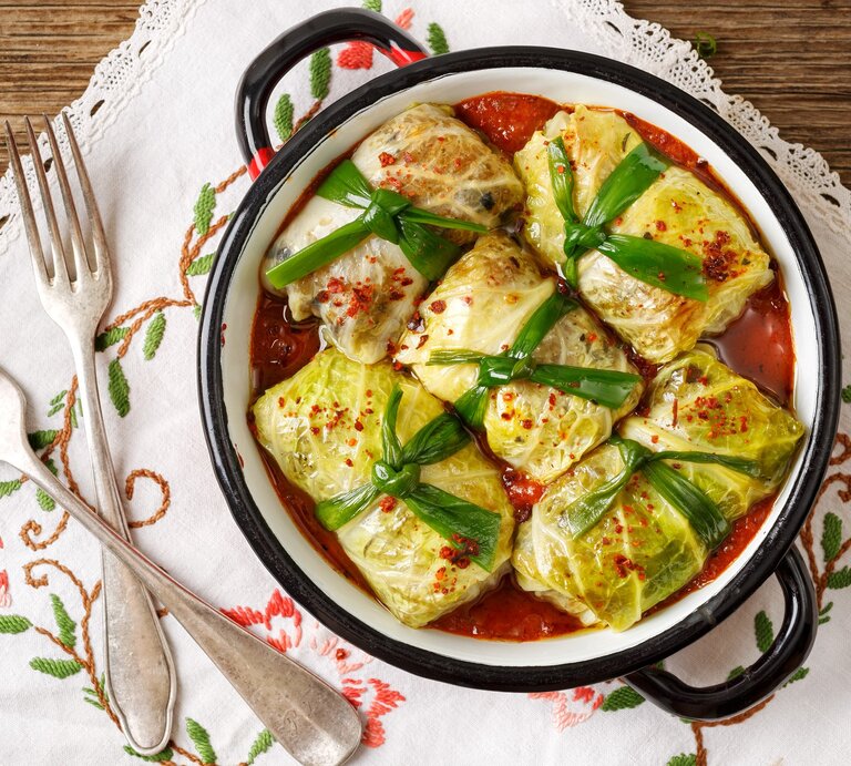 Frisch gemachte vegetarische Kohlrouladen in einem Topf / jede ist mit einem breitem band verschnürt / Untergrund besticktes Tuch auf Holz / Zwei gabeln / Draufsicht | © iStock/zi3000