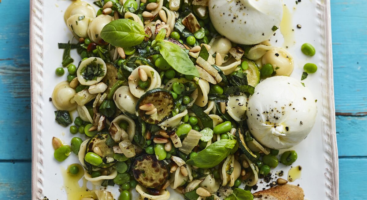 Der grüne Nudelsalat mit Burrata auf einem viereckigen, weißen Teller. Alles direkt von oben fotografiert.