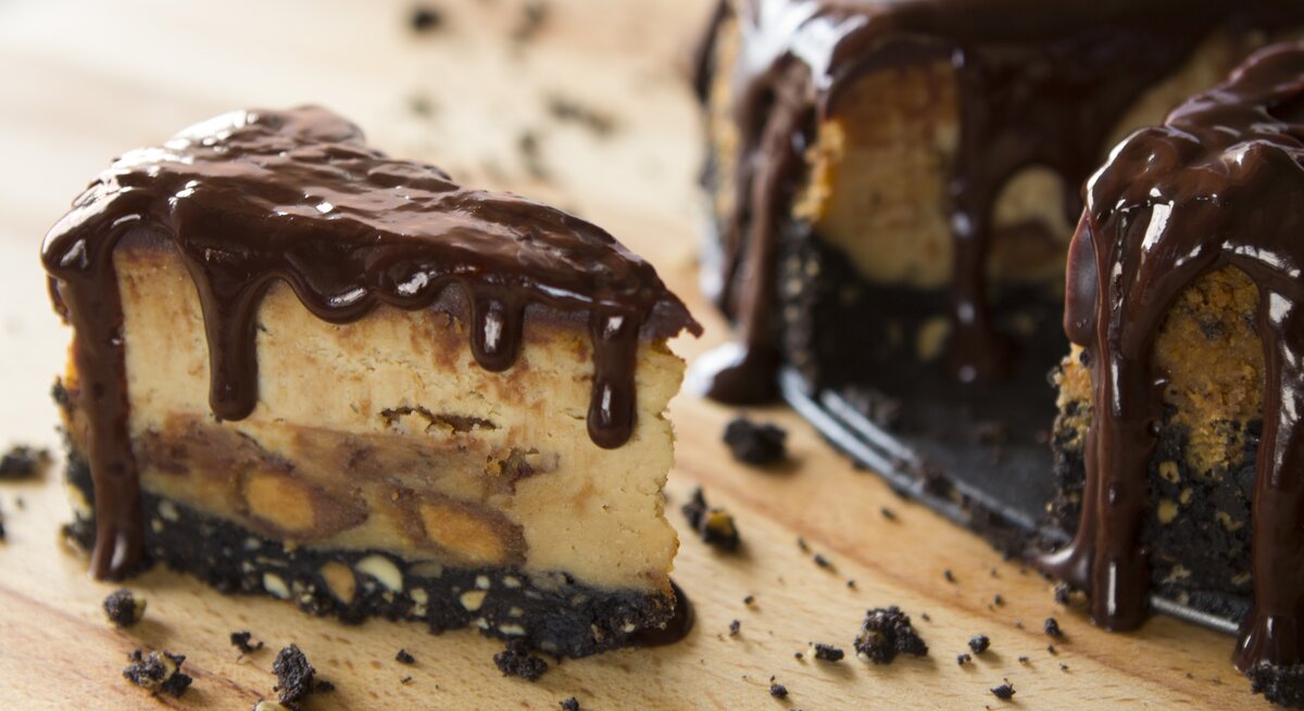 Erdnussbutter-Käsekuchen mit flüssiger Schokosoße auf hölzernem Untergrund.