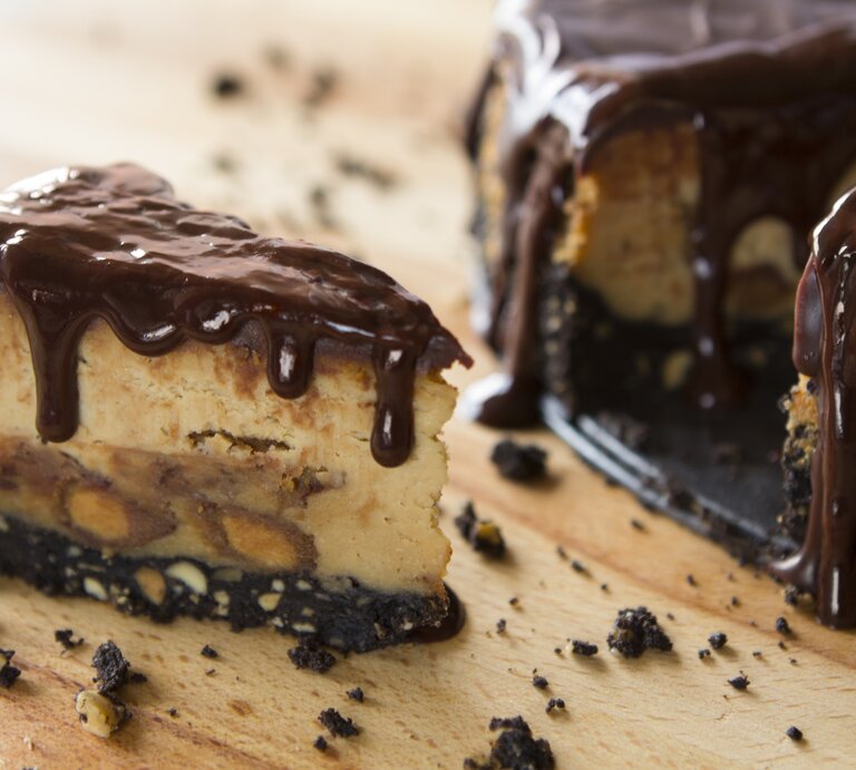 Erdnussbutter-Käsekuchen mit flüssiger Schokosoße auf hölzernem Untergrund. | © GettyImages/youngvet