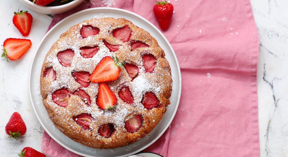 Ansicht von oben auf frisch gebackenen Erdbeerkuchen. Alles auf weißem Marmortisch mit rosa Tischdecke. | © Shutterstock/zoryanchik