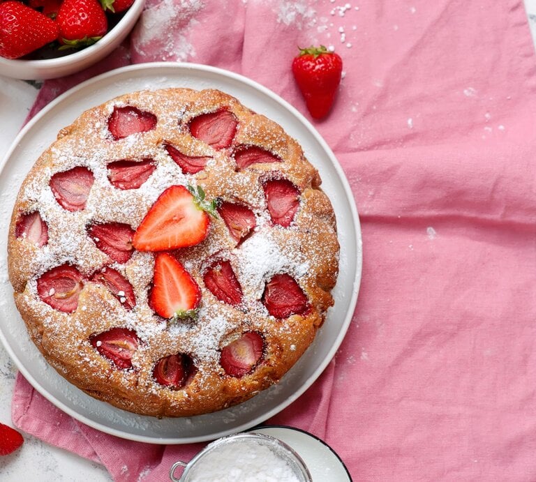Ansicht von oben auf frisch gebackenen Erdbeerkuchen. Alles auf weißem Marmortisch mit rosa Tischdecke. | © Shutterstock/zoryanchik