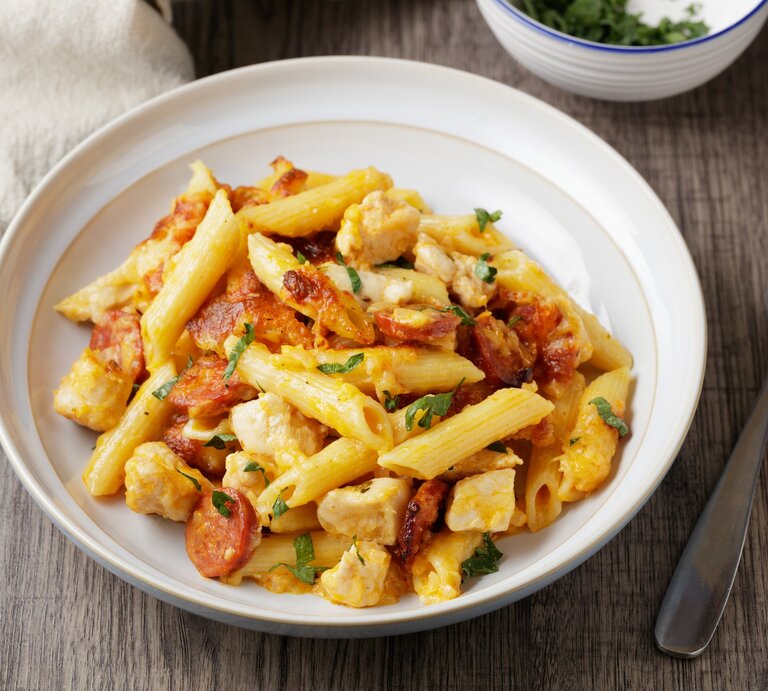 Pasta mit Bärlauch, Chorizo und Hähnchenbrust in weißem Pastateller auf Holz. Daneben eine Schale mit Bärlaich, ein Tuch und eine Gabel. Draufsicht. | © Getty Images / haoliang