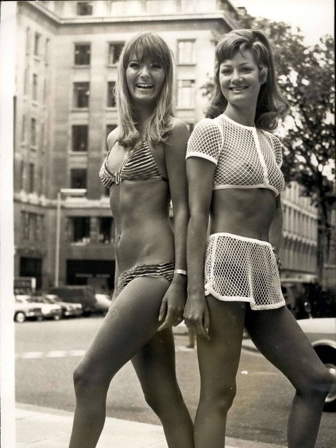 Zwei junge Frauen in Bademode der 1960er-Jahre, eine im Bikini und die andere im Netzoberteil, posieren lächelnd auf einer Straße in der Stadt. | © imago/ZUMA/Keystone