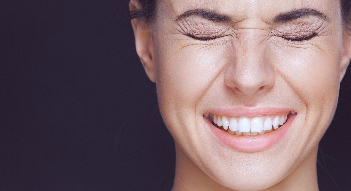 Frau, die die Augen fest geschlossen hat und lächelt. Man sieht ihre weißen Zähne, und sie scheint entweder zu lachen oder einen intensiven Moment zu erleben.