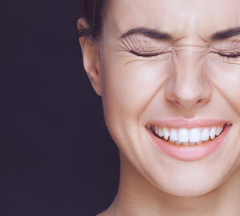 Frau, die die Augen fest geschlossen hat und lächelt. Man sieht ihre weißen Zähne, und sie scheint entweder zu lachen oder einen intensiven Moment zu erleben. | © iStock/gruizza