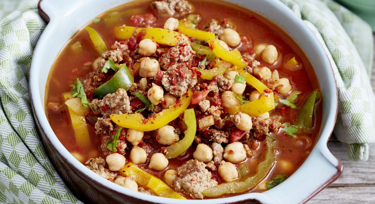 Orientalischer Kichererbseneintopf mit Paprika, Chili, Hackfleisch und Kichererbsen in einer hellen Form auf einem Holztisch