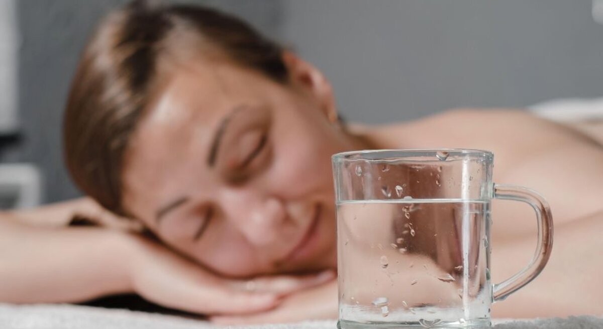 Eine Frau liegt antspannt auf einer Massageliege. Im Vordergrund ein Glas Wasser