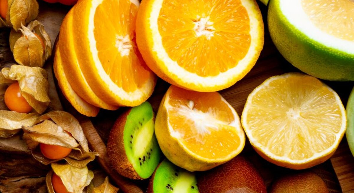 Aufgeschnittene Orangen, Grapefruit, Kiwi und Physalis liegen nebeneinander auf einem Holzuntergrund und zeigen eine Auswahl vitamin-C-reicher Früchte.