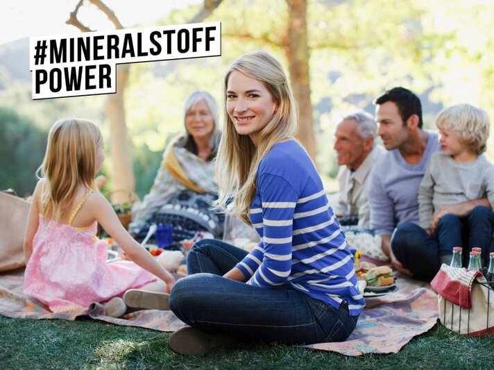 Frau um die 40 sitzt auf Picknickdecke umgeben von anderen Personen | © iStock/Paul Bradbury