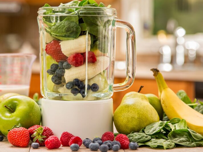 Mixer mit frischem Obst und Gemüse: Bananen, Beeren, Spinat, Äpfel und Birnen liegen auf der Arbeitsplatte und im Glasbehälter – Zutaten für einen gesunden Smoothie. | © Getty Images Signature/  Janine Lamontagne