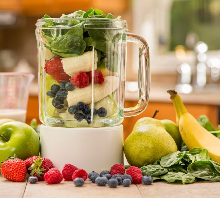 Mixer mit frischem Obst und Gemüse: Bananen, Beeren, Spinat, Äpfel und Birnen liegen auf der Arbeitsplatte und im Glasbehälter – Zutaten für einen gesunden Smoothie. | © Getty Images Signature/  Janine Lamontagne