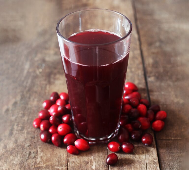 Ein Glas dunkler Cranberrysaft steht auf rustikalem Holztisch, umgeben von frischen roten Cranberries. | © stock.adobe.com/Printemps