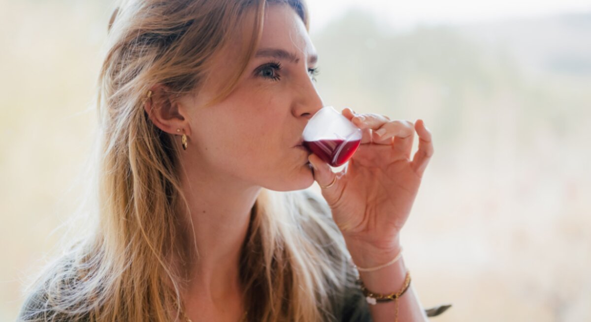 Blondhaarige Frau trinkt genüsslich den Saft EisenPlus vor einem hellen, verschwommenen Waldpanorama.
