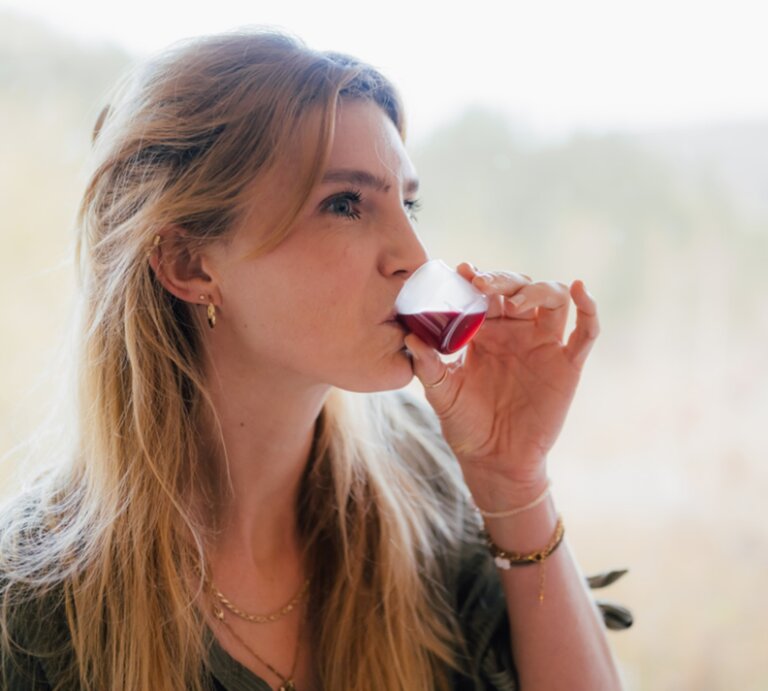 Blondhaarige Frau trinkt genüsslich den Saft EisenPlus vor einem hellen, verschwommenen Waldpanorama. | © Rabenhorst
