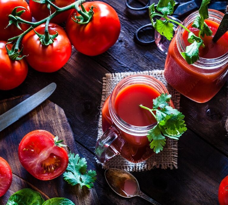 Ein Tisch aus Holz mit einem Brettchen, auf dem ein Messer liegt. Tomaten liegen auf dem Tisch und ein Glas mit Tomatensaft ist von Oben zu sehen.  | © Getty Images/fcafotodigital