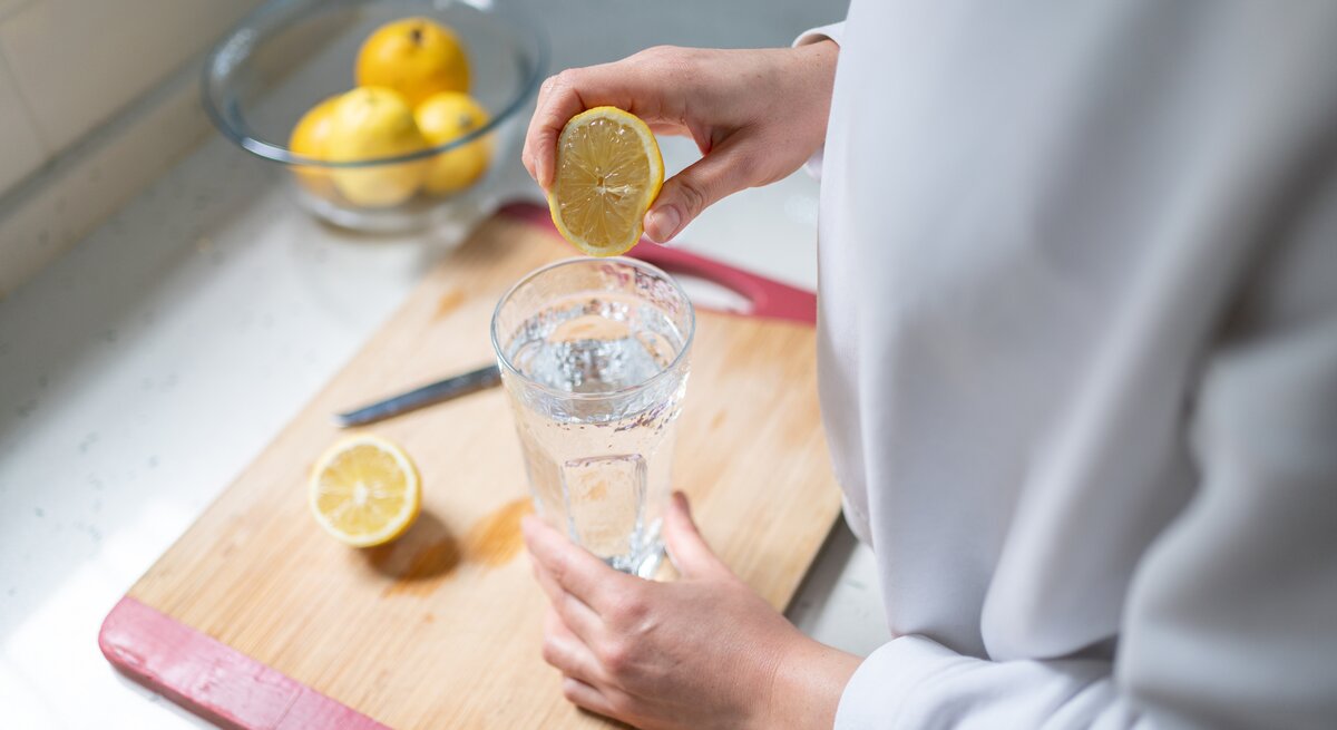 Eine Frau presst den Saft einer halben Zitrone in ein Glas.
