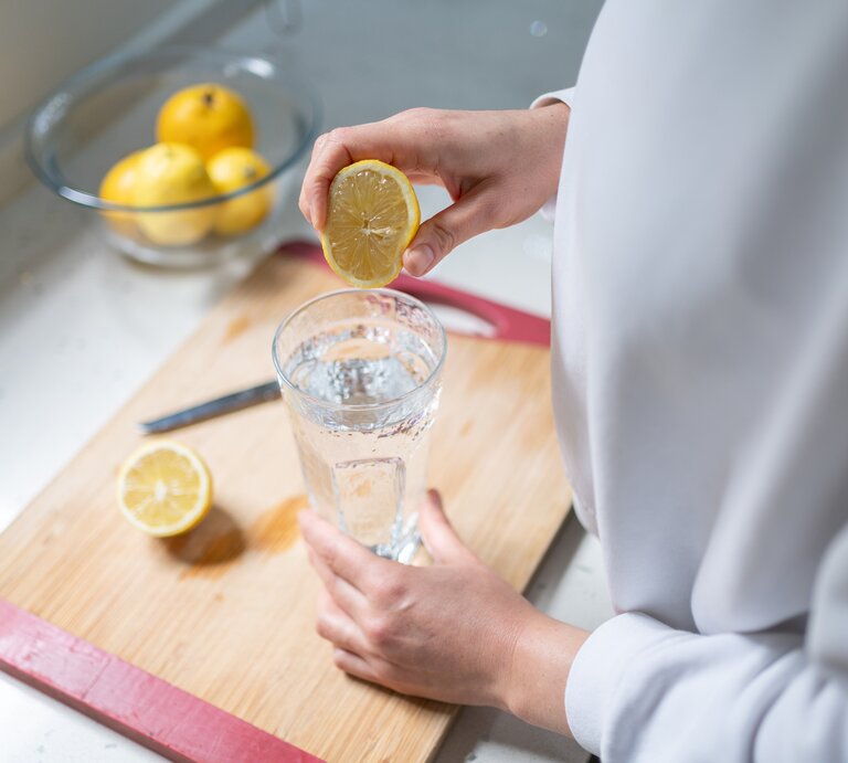 Eine Frau presst den Saft einer halben Zitrone in ein Glas. | © Getty Images