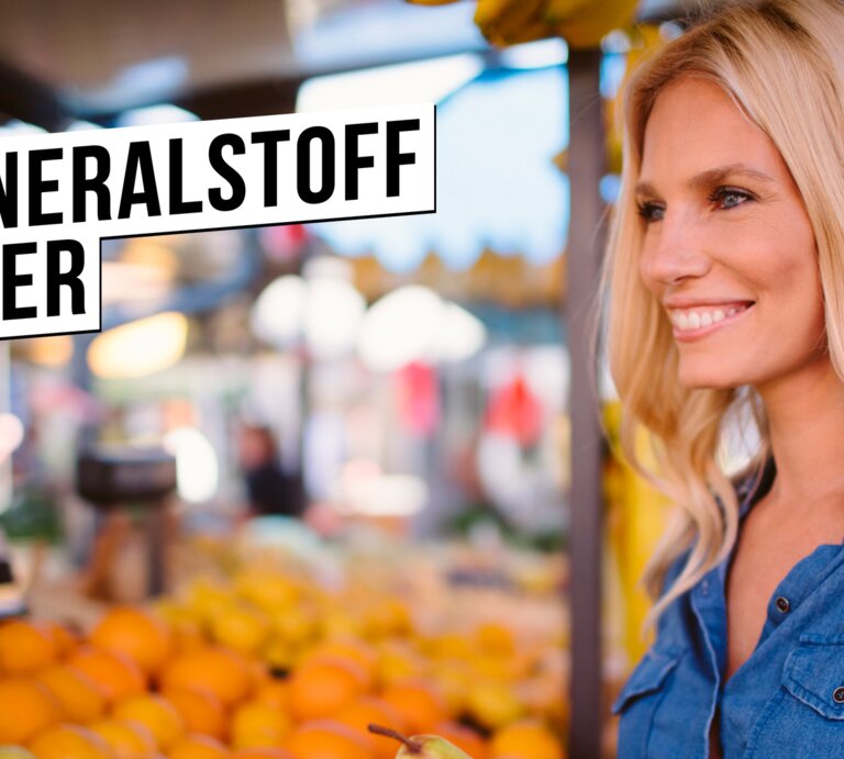 Junge blonde Frau in Jeanshemd lächelt zufrieden beim Auswählen von Birnen an einem bunten Obststand auf dem Wochenmarkt. | © istock.com/vgajic