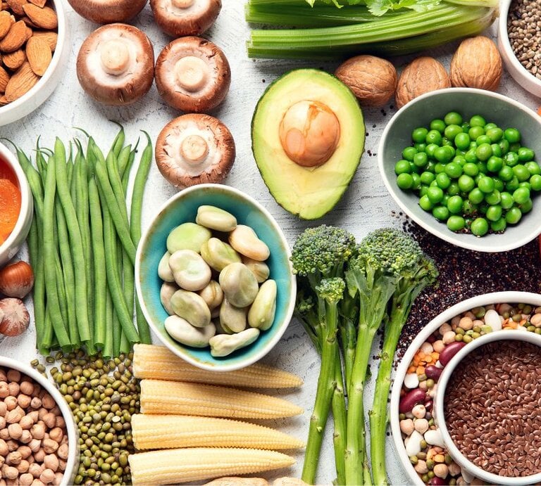 Von oben fotografierte Vielfalt pflanzlicher Lebensmittel—Erbsen, Bohnen, Linsen, Avocado, Brokkoli, Pilze, grüne Bohnen, Nüsse, Samen und Babymais—auf hellem Untergrund. | © Adobe Stock/ bit24