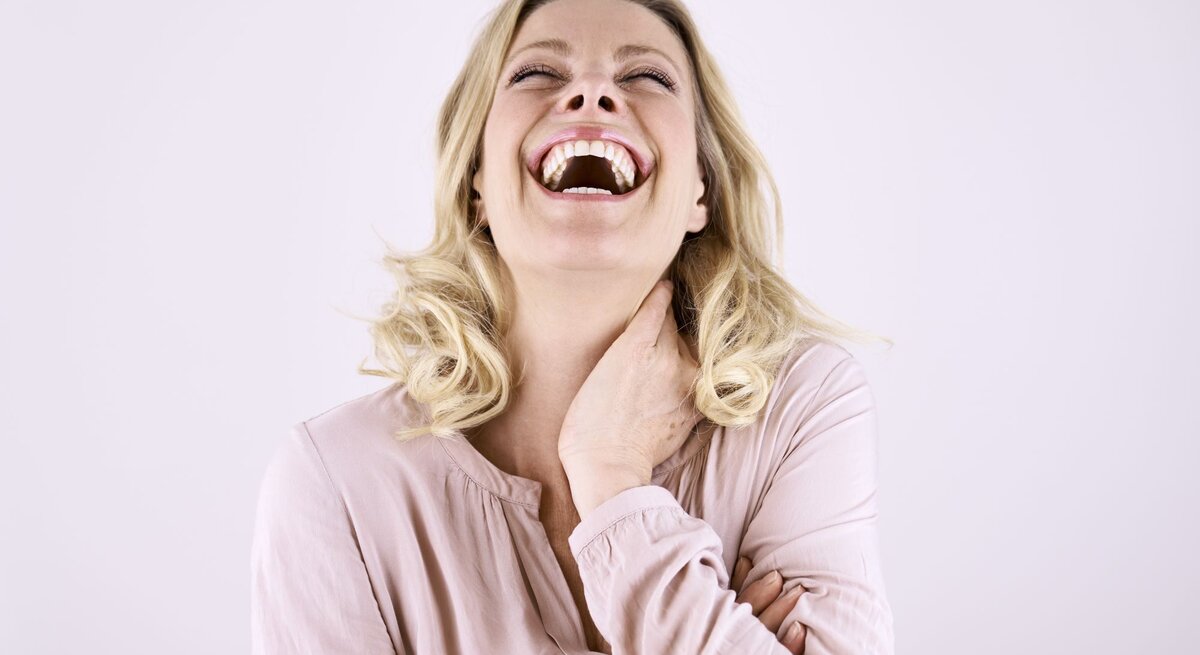 Blonde, junge Frau lacht herzhaft. 