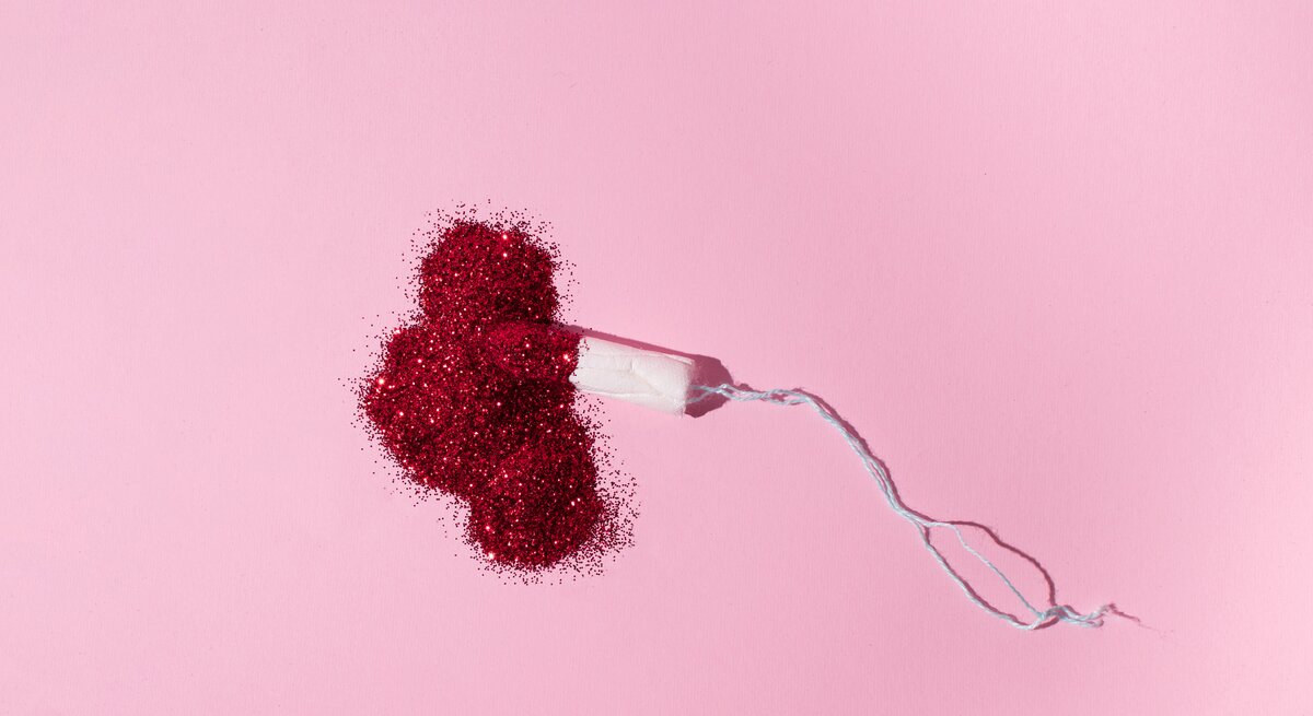 Tampon liegt auf rosa Untergrund in einem Haufen aus rotem Glitzer.