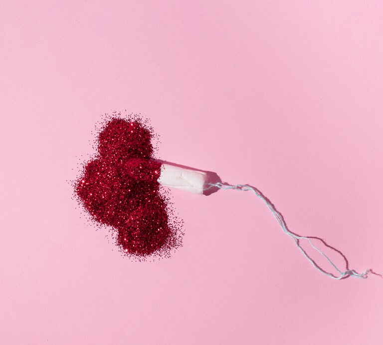 Tampon liegt auf rosa Untergrund in einem Haufen aus rotem Glitzer. | © Getty Images/ Helena Nikolic