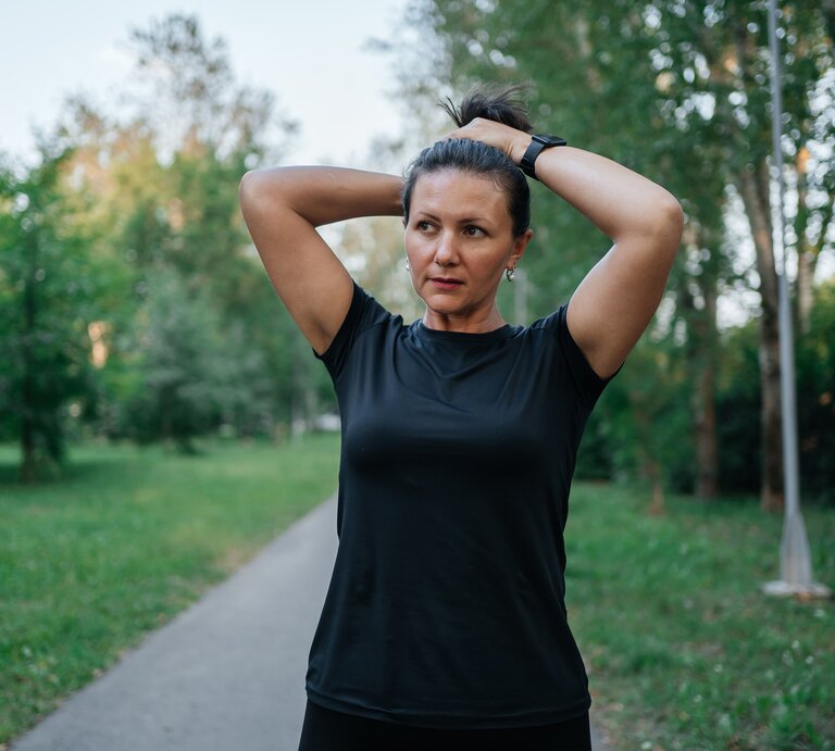 Frau über 45 bindet sich die Haare zum Zopf, ihre Stirn glänzt. | © Getty Images/ Svetlana Repnitskaya