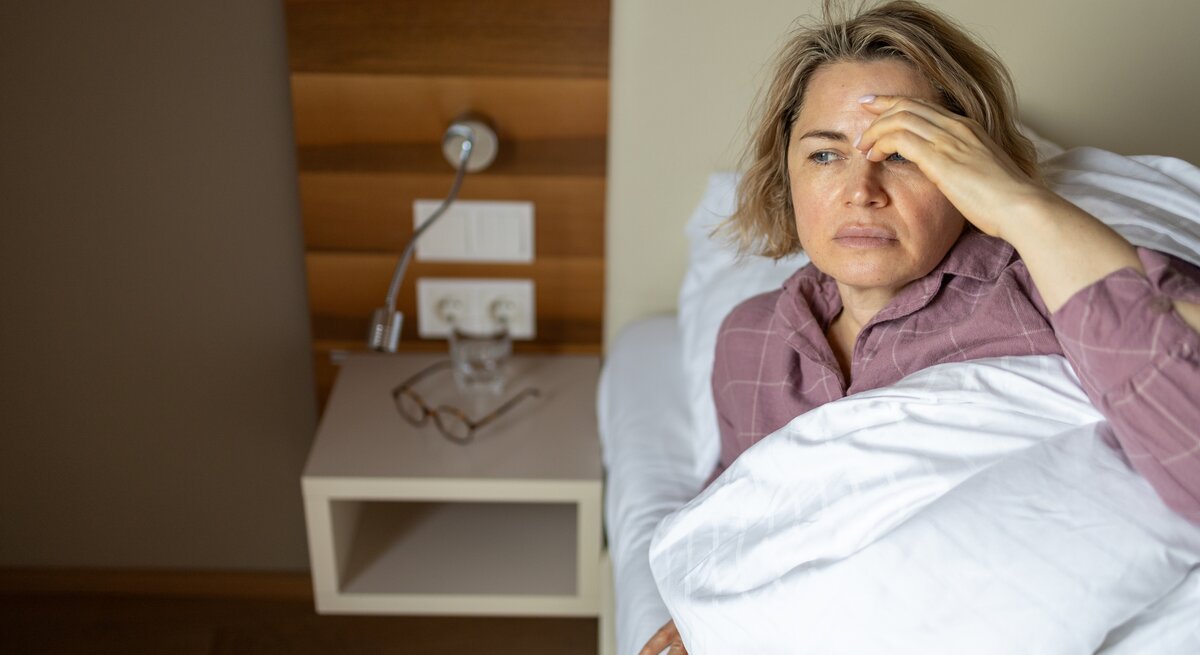 Frau liegt im Bett, ihre Stirn glänzt.