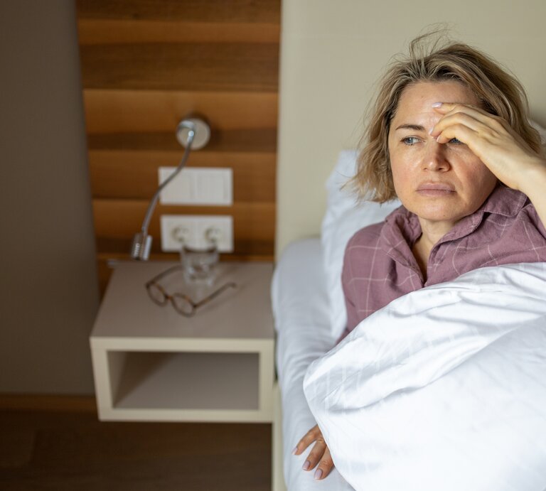 Frau liegt im Bett, ihre Stirn glänzt. | © Getty Images/ Kate Wieser