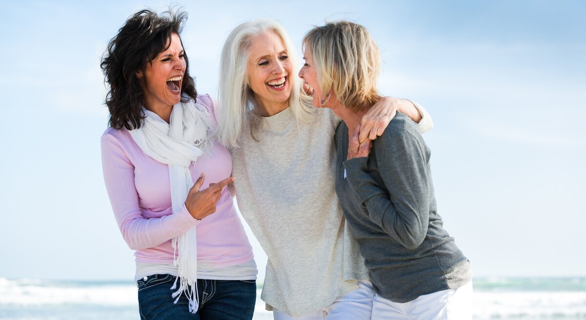 Porträt von drei Frauen am Strand, die lachen und Spaß haben.