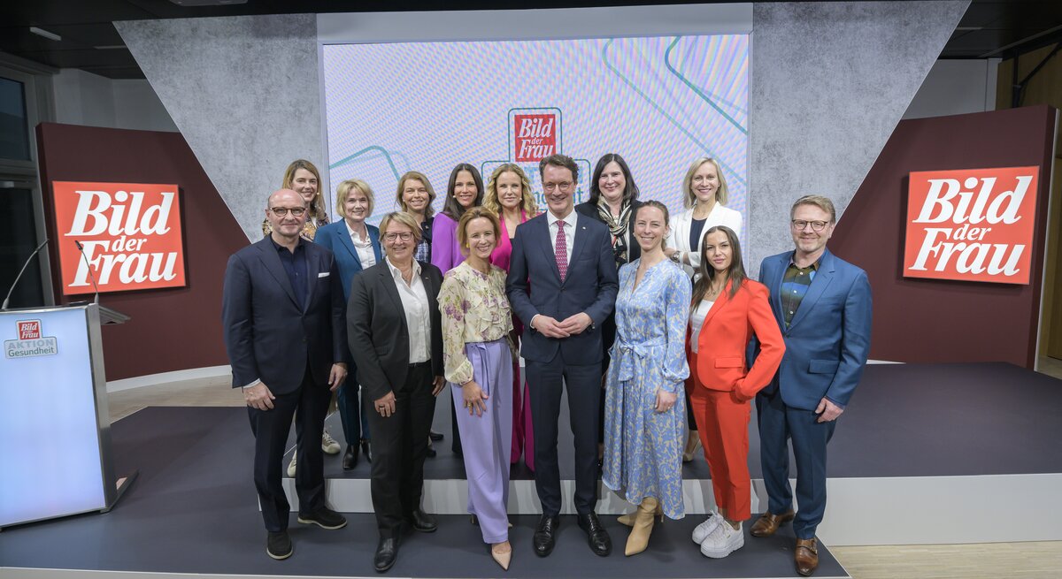 Vierzehn Frauen und zwei Männer in Businesskleidung posieren lächelnd auf einer Bühne vor „Bild der Frau“-Logos.