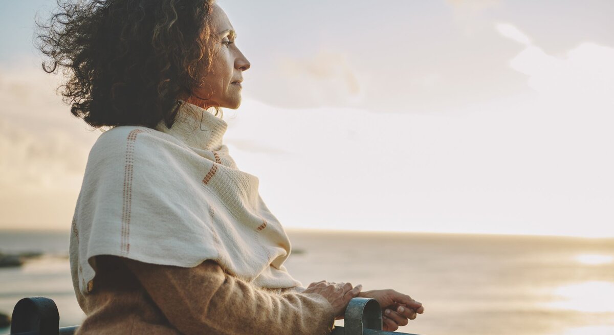 Eine Frau steht am Strand und guckt in den Sonnenaufgang über dem Meer.