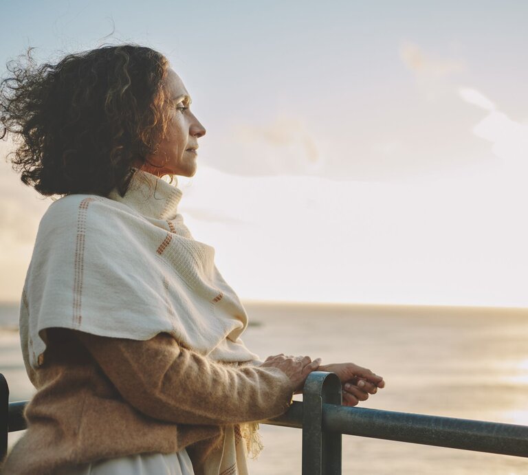 Eine Frau steht am Strand und guckt in den Sonnenaufgang über dem Meer. | © iStock